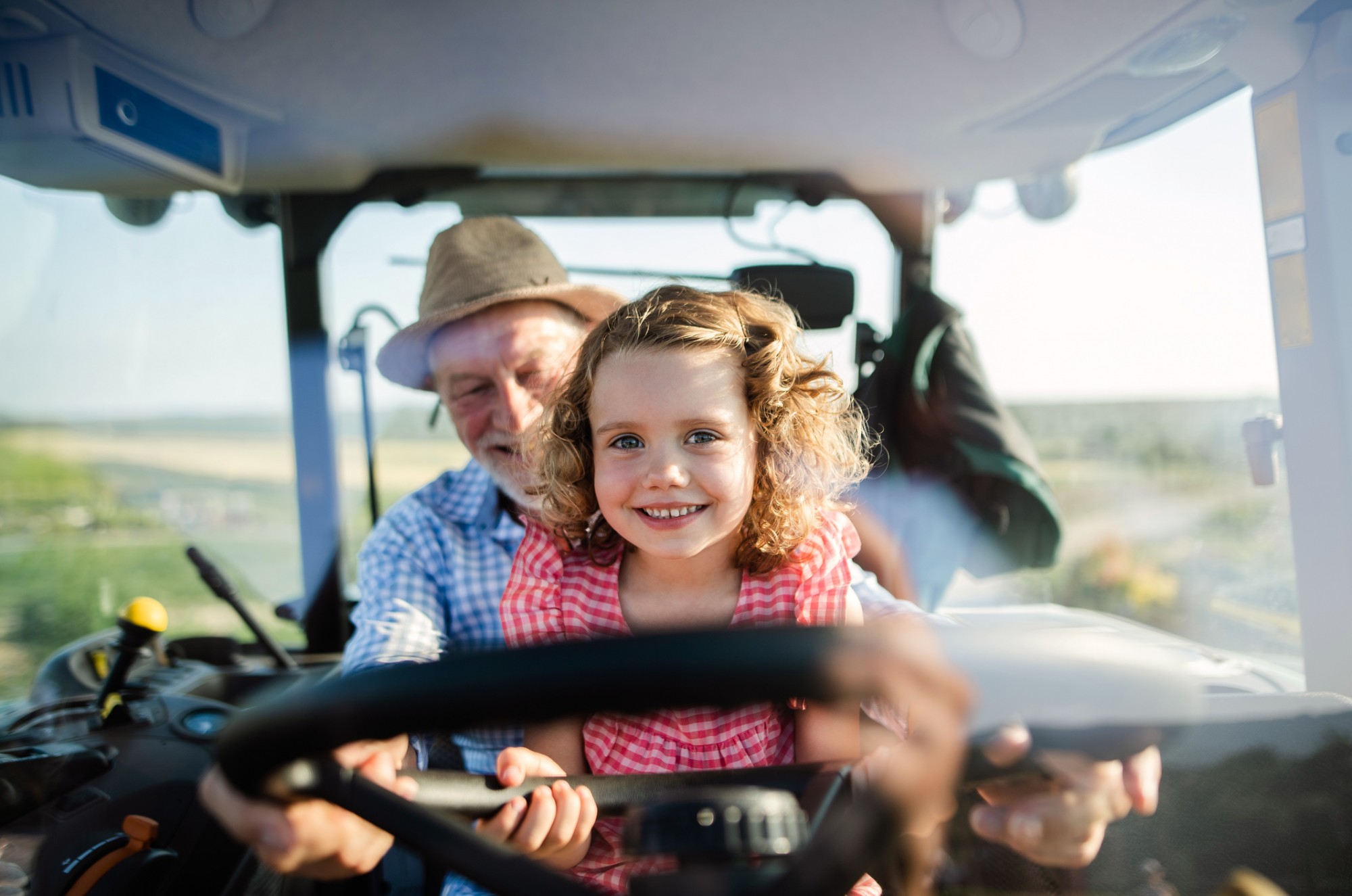 grandfather and granddaughter driving tractor in field